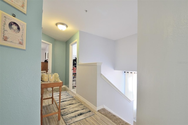 hall with light wood-type flooring, baseboards, and an upstairs landing