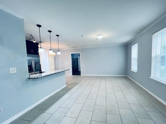 kitchen featuring light stone counters, a sink, baseboards, stainless steel fridge, and crown molding