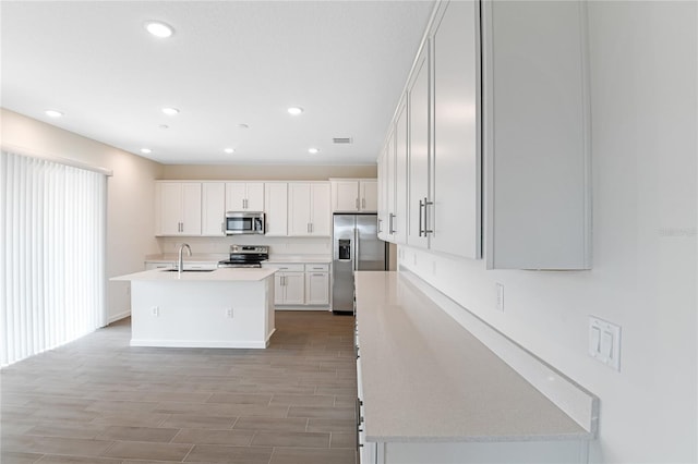 kitchen with white cabinets, sink, an island with sink, appliances with stainless steel finishes, and light hardwood / wood-style floors