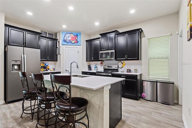 kitchen featuring a kitchen island with sink, appliances with stainless steel finishes, a breakfast bar, sink, and light hardwood / wood-style floors