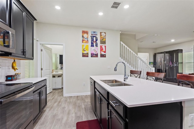 kitchen with decorative backsplash, light hardwood / wood-style flooring, a center island with sink, stainless steel appliances, and sink