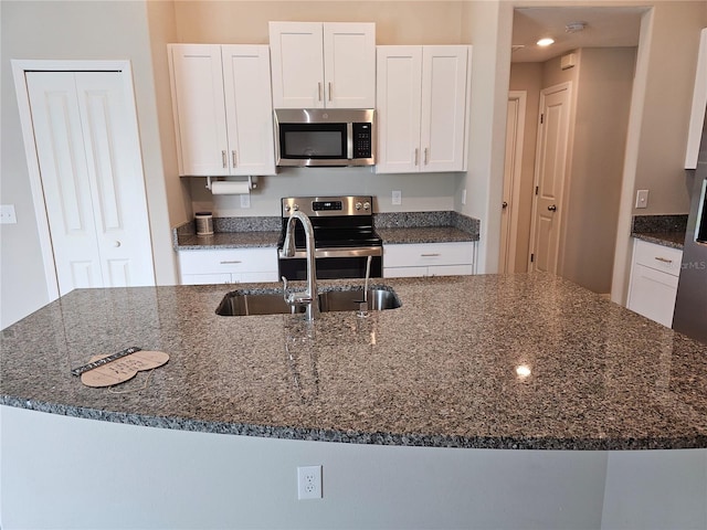 kitchen featuring white cabinetry, dark stone counters, appliances with stainless steel finishes, and a sink