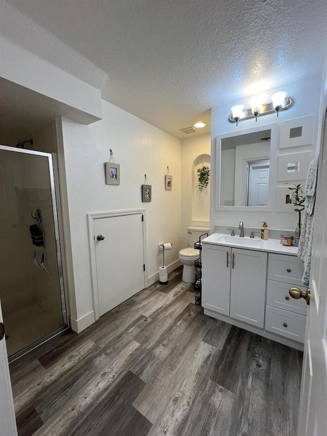 bathroom with toilet, a stall shower, a textured ceiling, vanity, and wood finished floors