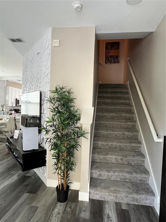 stairs featuring a textured ceiling, visible vents, and wood finished floors