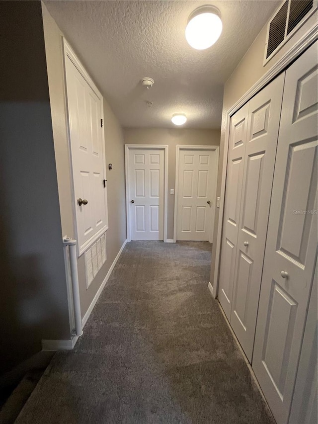 corridor featuring baseboards, visible vents, dark carpet, and a textured ceiling