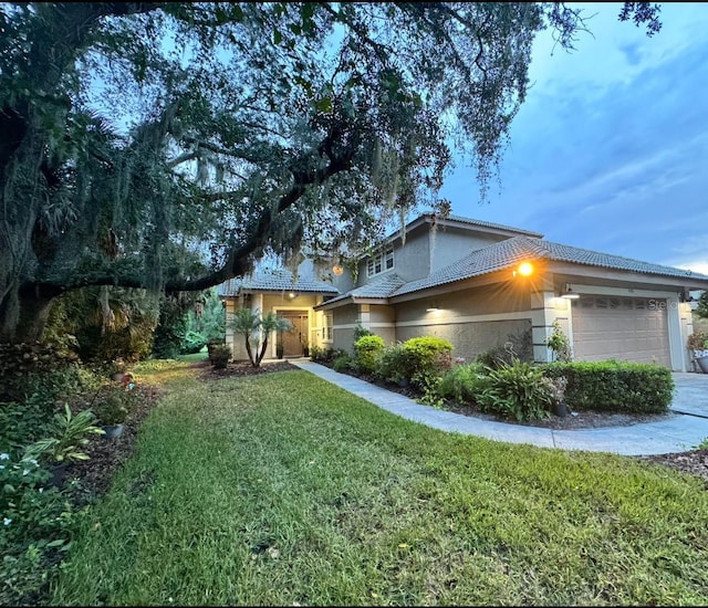 view of home's exterior featuring a yard, an attached garage, a tiled roof, and stucco siding