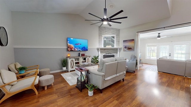 living room with baseboards, lofted ceiling, ceiling fan, wood finished floors, and a stone fireplace