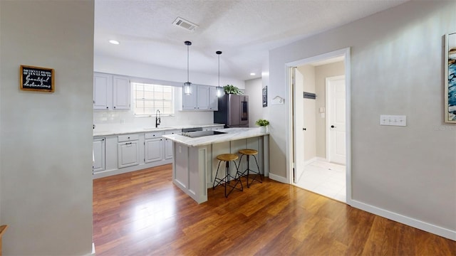 kitchen with sink, stainless steel fridge with ice dispenser, backsplash, kitchen peninsula, and a breakfast bar