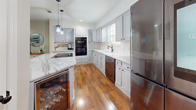 kitchen with light stone counters, sink, black appliances, wine cooler, and hanging light fixtures