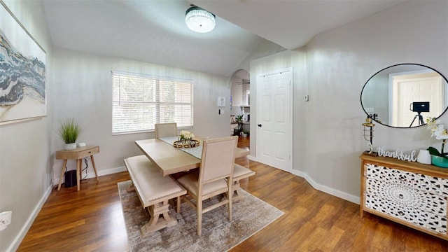 dining space with baseboards, arched walkways, vaulted ceiling, and wood finished floors