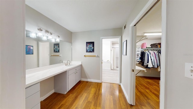 bathroom with baseboards, visible vents, wood finished floors, a spacious closet, and vanity