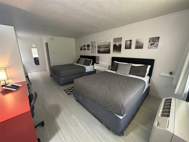 bedroom with light wood-style flooring, baseboards, and a textured ceiling