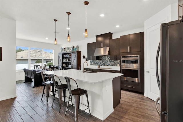 kitchen with a center island with sink, stainless steel appliances, tasteful backsplash, decorative light fixtures, and a kitchen breakfast bar