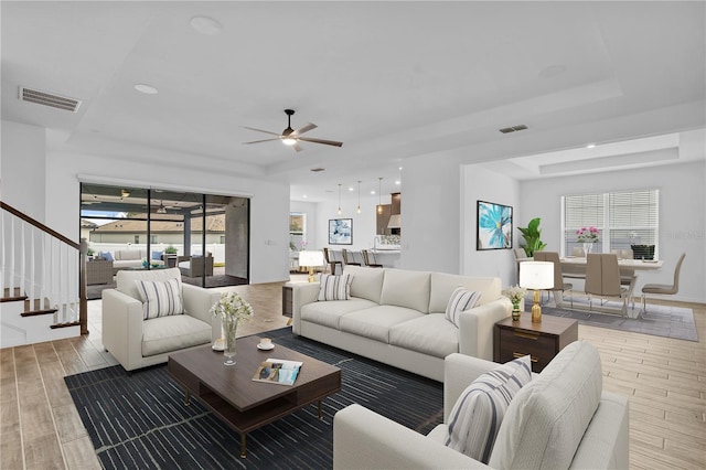 living room featuring ceiling fan, a tray ceiling, and light hardwood / wood-style floors