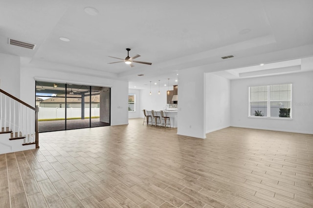 unfurnished living room featuring a tray ceiling and ceiling fan