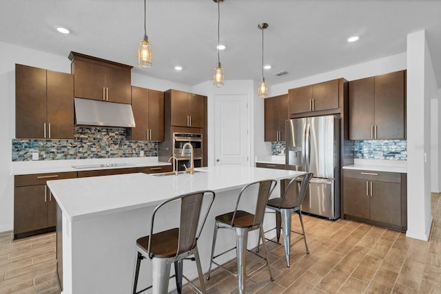 kitchen with dark brown cabinetry, appliances with stainless steel finishes, and a center island with sink