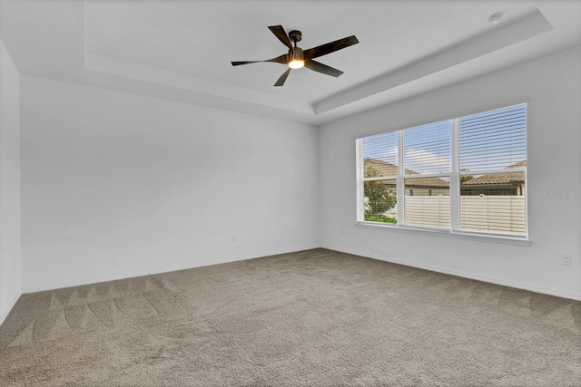 carpeted spare room with a tray ceiling and ceiling fan