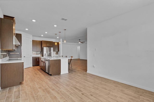 kitchen with light hardwood / wood-style flooring, hanging light fixtures, appliances with stainless steel finishes, a kitchen island, and backsplash