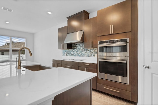 kitchen featuring black electric cooktop, sink, double oven, and a center island with sink