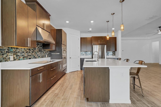 kitchen with sink, a breakfast bar area, stainless steel fridge, an island with sink, and pendant lighting