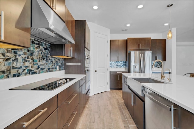 kitchen featuring extractor fan, appliances with stainless steel finishes, sink, hanging light fixtures, and light hardwood / wood-style flooring