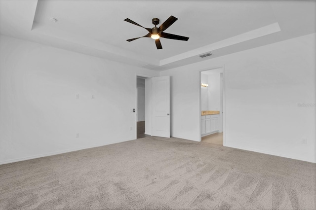 carpeted empty room with ceiling fan and a raised ceiling