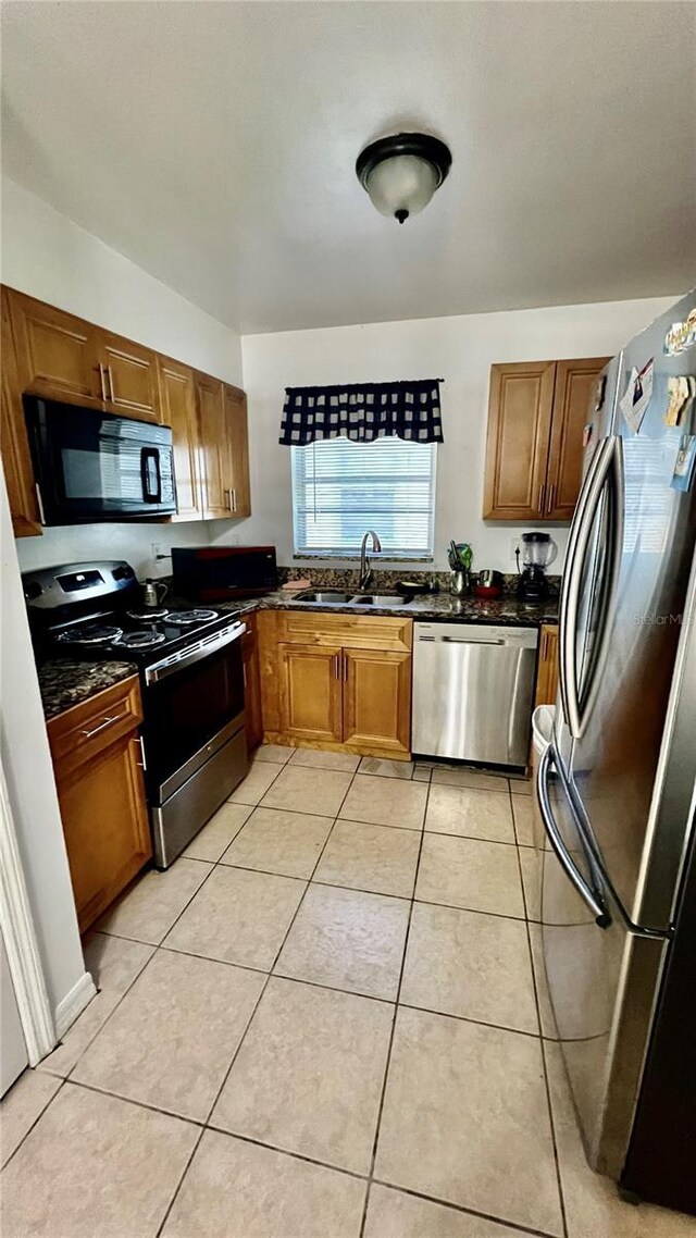 kitchen featuring dark stone counters, light tile patterned flooring, stainless steel appliances, and sink