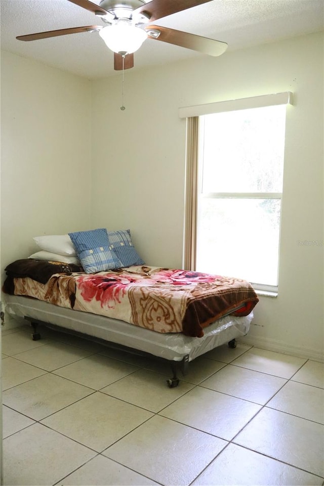 bedroom featuring ceiling fan, light tile patterned floors, and a textured ceiling