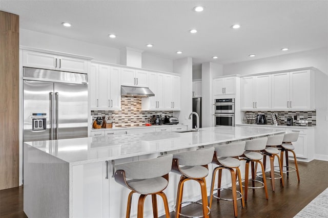 kitchen with white cabinetry, a kitchen bar, a large island, light stone counters, and stainless steel appliances