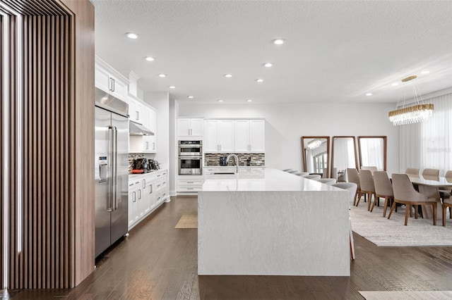 kitchen featuring appliances with stainless steel finishes, white cabinetry, dark hardwood / wood-style floors, tasteful backsplash, and a kitchen island with sink