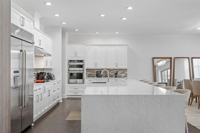 kitchen with sink, dark wood-type flooring, appliances with stainless steel finishes, white cabinetry, and an island with sink