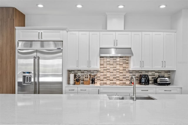 kitchen with white cabinets, tasteful backsplash, built in fridge, and sink