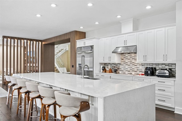 kitchen with sink, built in refrigerator, a kitchen breakfast bar, white cabinets, and a large island with sink