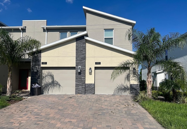 view of side of home with an attached garage, stone siding, decorative driveway, and stucco siding