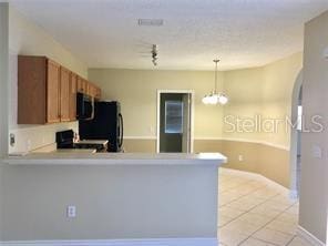 kitchen featuring kitchen peninsula, light tile patterned flooring, black range oven, and hanging light fixtures