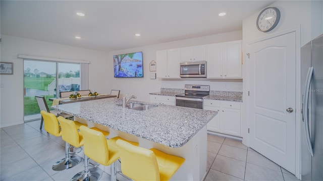 kitchen featuring stainless steel appliances, white cabinets, a center island with sink, sink, and light stone counters