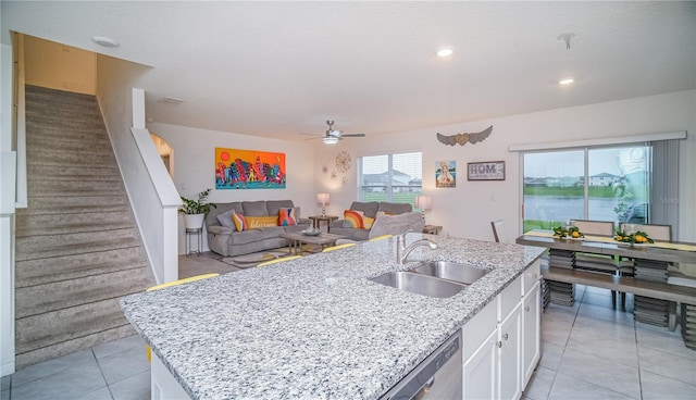kitchen with light stone counters, a sink, white cabinets, open floor plan, and a center island with sink