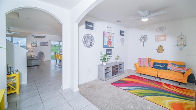 interior space with arched walkways, a ceiling fan, light carpet, light tile patterned flooring, and baseboards