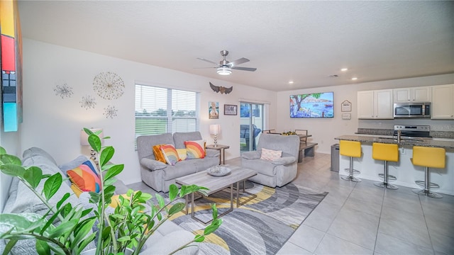 living area with a textured ceiling, light tile patterned floors, recessed lighting, a water view, and a ceiling fan