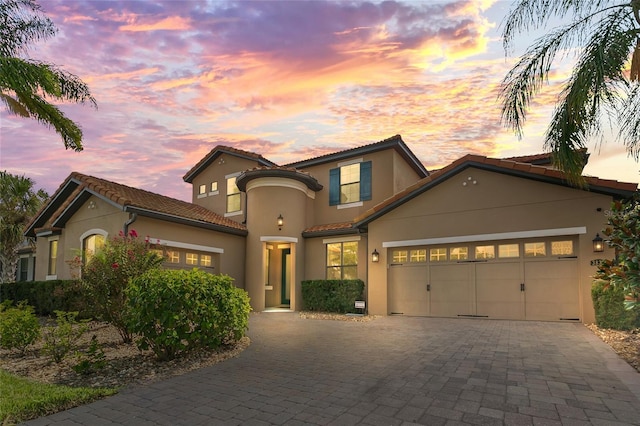 mediterranean / spanish house featuring decorative driveway, an attached garage, and stucco siding