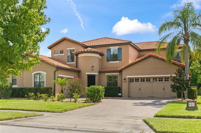 mediterranean / spanish-style home with driveway, a garage, stucco siding, a tiled roof, and a front yard