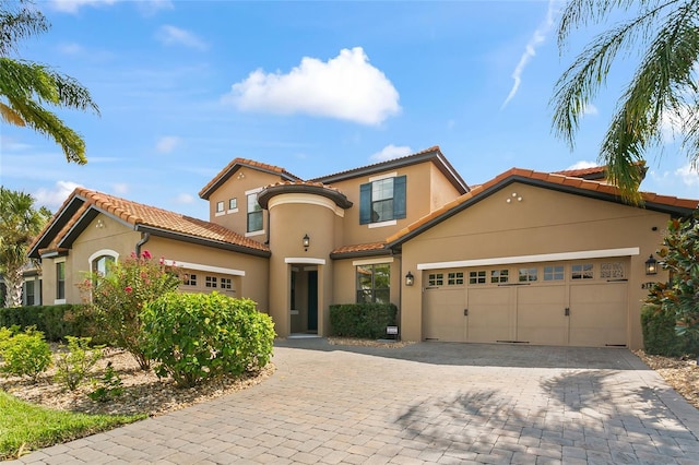 mediterranean / spanish-style home with a garage, a tiled roof, decorative driveway, and stucco siding