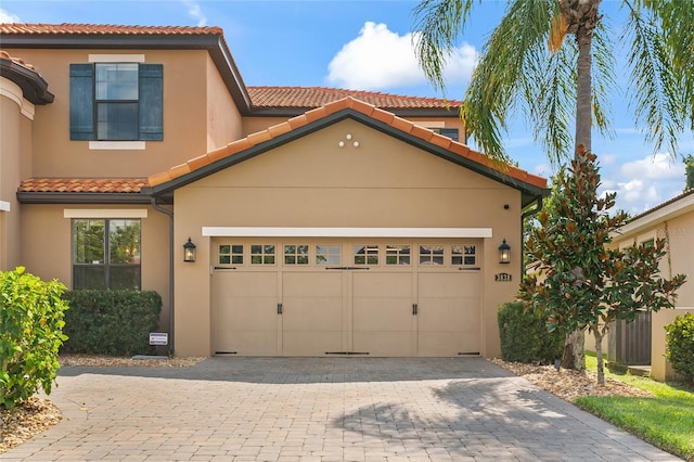 view of front of property featuring a garage, decorative driveway, a tile roof, and stucco siding