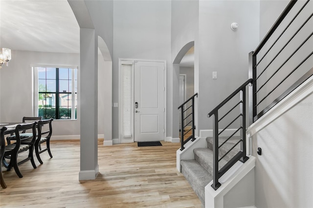 entryway featuring baseboards, arched walkways, stairs, light wood-style floors, and a notable chandelier