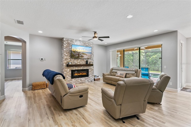 living room featuring arched walkways, a fireplace, visible vents, a textured ceiling, and light wood-type flooring