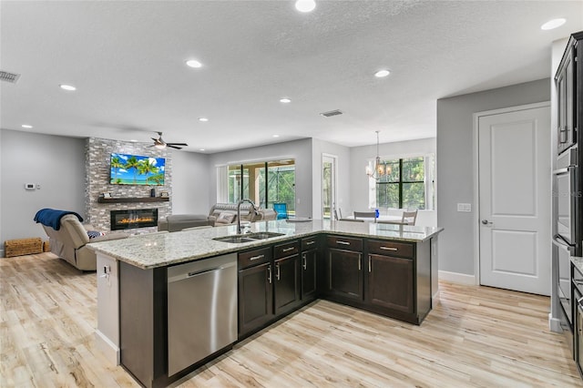 kitchen featuring dishwasher, light hardwood / wood-style flooring, sink, light stone counters, and a fireplace