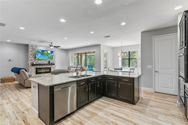 kitchen with a fireplace, a sink, light wood-style floors, open floor plan, and dishwasher