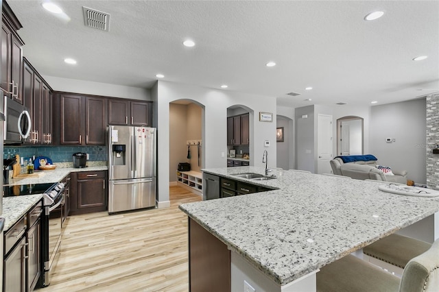 kitchen featuring arched walkways, stainless steel appliances, visible vents, a sink, and dark brown cabinetry