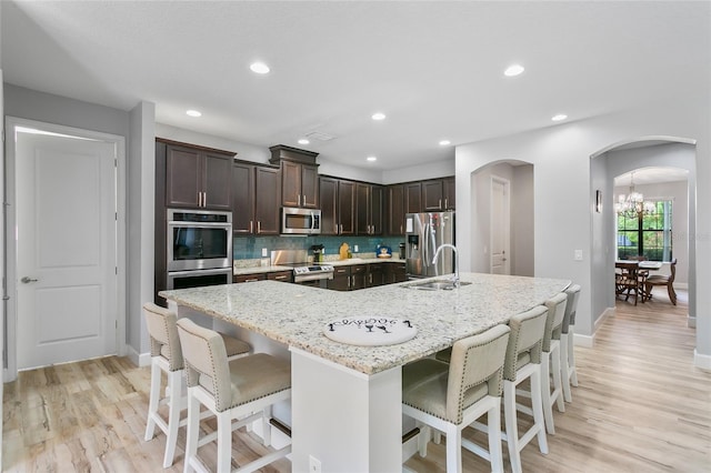 kitchen featuring backsplash, a breakfast bar, appliances with stainless steel finishes, light hardwood / wood-style floors, and sink