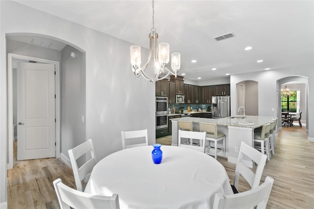 dining space with light wood-type flooring, sink, and an inviting chandelier